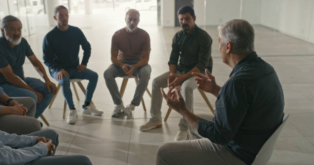 istock Men talking and sharing their struggles with addiction during a AA meeting while sitting on chairs during group therapy. Diverse businessmen having a discussion or debate in an office with lens flare 1411325535