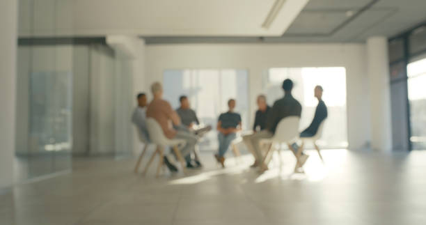 Blurred people in group therapy session. Addicts talking and sharing during physiotherapy while sitting on chairs in a community center or rehab. Businesspeople doing team building or AA meeting