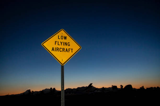 日の出または日の入り時に撮影された低空飛行航空機の警告を示す黄色い標識の水平画像 - airplane stunt yellow flying ストックフォトと画像
