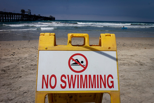 A sign at a beach stating No Swimming in red letters