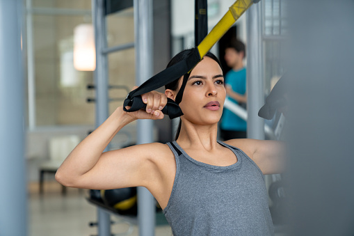 Fit Latin American woman training at the gym using TRX straps - fitness concepts