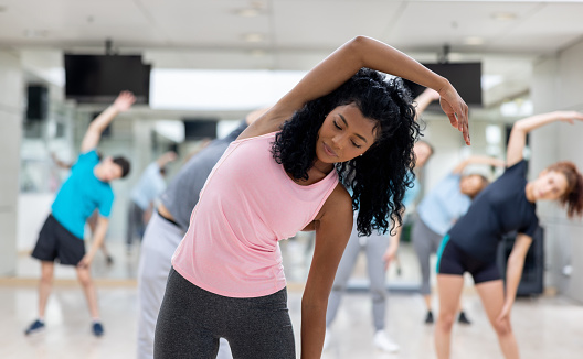 African American female fitness instructor guiding an exercise class at the gym and stretching - healthy lifestyle concepts