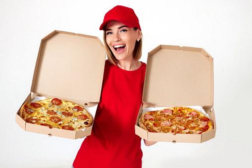 Friendly pizza delivery girl in red uniform showing opened boxes with delicious pizza on white background. choice