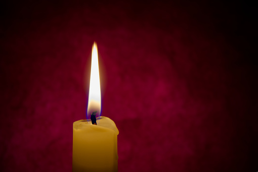 Single red candle burning alone in the dark red background. Conceptual image symbolize peace, love, hope or patience with free copy space