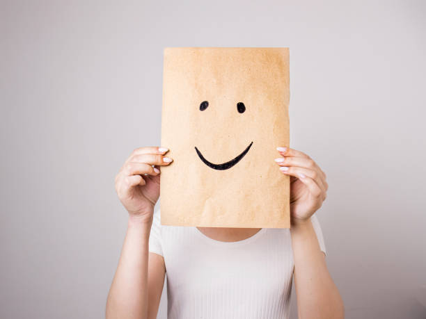 woman holding paper with a painted smile in front of her face woman holding paper with a painted smile in front of her face, selective focus cheesy grin stock pictures, royalty-free photos & images