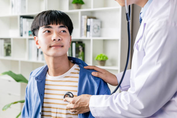 Doctor hold stethoscope listen to teenager boy patient heart in stock photo