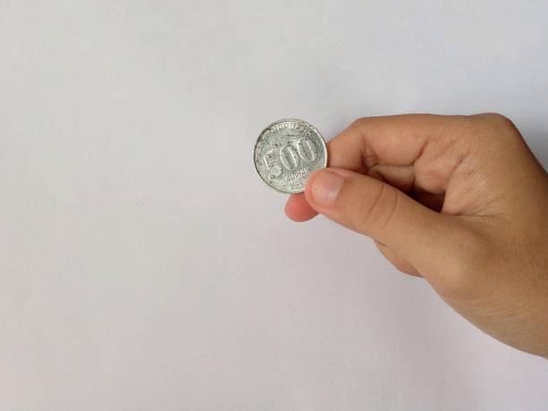 istock Hand holding a slightly worn 500 rupiah coin on a white background 1411344928