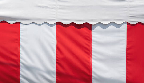Red and white striped canvas awning and white roof tent with sunlight on surface
