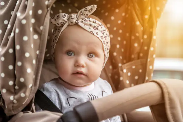 Photo of Portrait curious surprised emotional eight-month-old blue-eyes girl sitting in stroller looking away