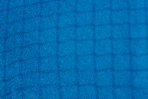 Colorful sports court background. Top view light blue field rubber ground with shadow from football goal net in sunny day outdoors.