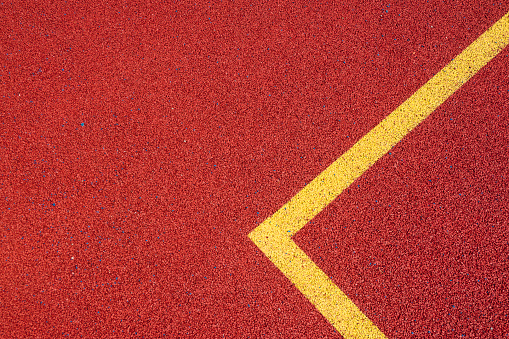 Colorful sports court background. Top view to red field rubber ground with yellow corner lines outdoors.
