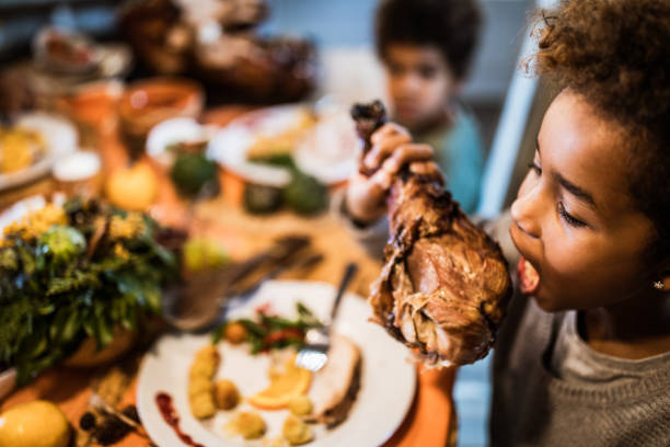 ragazza afroamericana che morde la coscia di tacchino durante il pranzo in sala da pranzo. - turkey leg foto e immagini stock