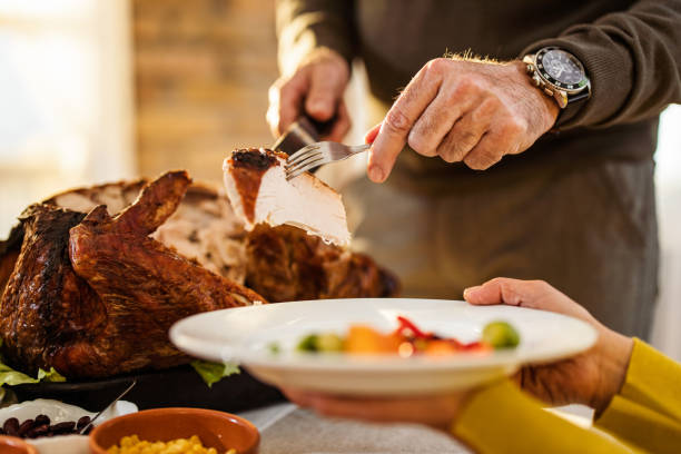 Unrecognizable man carving turkey meat and putting it on a plate at home.