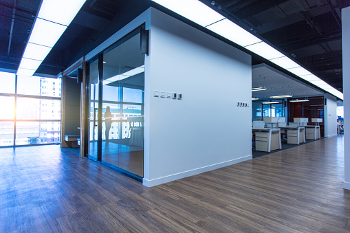 Empty office interior with copy space on carpet floor. Wordesks, lighting and computer equipment and windows in background behind glass door. Slight cross process effect added. 3D rendered image.