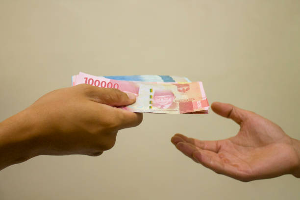mains donnant de l’argent - indonesian currency photos et images de collection