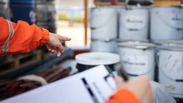 Action of a safety officer is point to chemical box at the factory storage area during perform safety audit, with the another hand is holding checklist paper (as blur foreground). Selective focus.