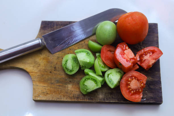 Red peppers and cherry tomatoes on green professional chopping board with knife - isolated on white background