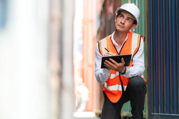 istock Dock worker man in safety vest holding tablet and looking at container to check defect in shipping yard. Import and export product. Manufacturing transportation and global business concept 1411366433