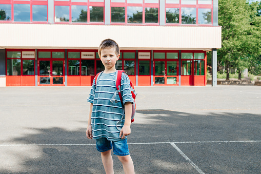 Portrait of a schoolboy with a backpack on his back standing against the backdrop of the school. The boy looks into the camera. Back to school.