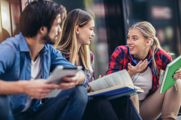 istock Group of happy university students talking while sitting outdoors at campus. 1411370159