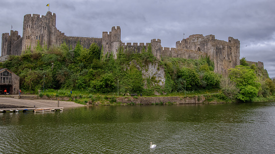 Pembroke Castle (Welsh: Castell Penfro) is a medieval castle in the centre of Pembroke, Pembrokeshire in Wales. The castle was the original family seat of the Earldom of Pembroke. A Grade I listed building since 1951, it underwent major restoration during the early 20th century.\n\nIn 1093, Arnulf of Montgomery built the first castle at the site when he fortified the promontory beside the Pembroke River during the Norman invasion of Wales.[3] A century later, the castle was given by Richard I to William Marshal, who became one of the most powerful men in 12th-century Britain. He rebuilt Pembroke Castle in stone, creating most of the structure that remains today.  Pembroke, United Kingdom.