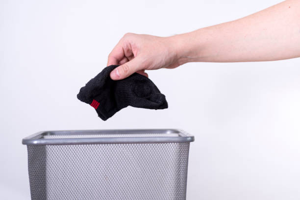 istock A man is throwing an old sock into a trash can with his hand against a white background. 1411373221