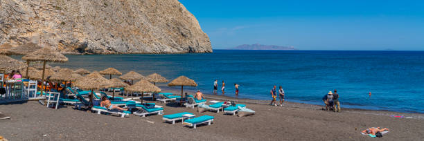 perissa schwarzer strand in santorini mit menschen im urlaub - black sand beach santorini greece stock-fotos und bilder