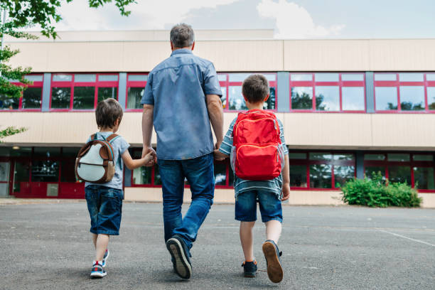 vuelta al cole. vista desde la espalda de un padre feliz acompaña a los escolares de sus hijos a la escuela. cuidado parental de los niños - school fotografías e imágenes de stock