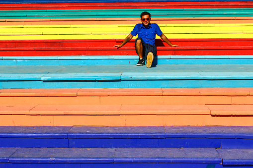 A young man enjoying the sun and the holidays on a rainbow painted staircase