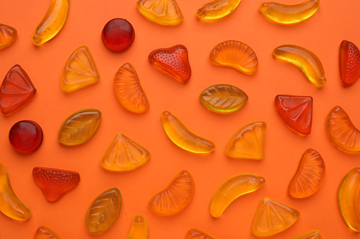 Delicious gummy fruit candies on orange background, flat lay