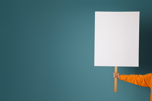 Woman holding blank sign on light blue background, closeup. Space for design