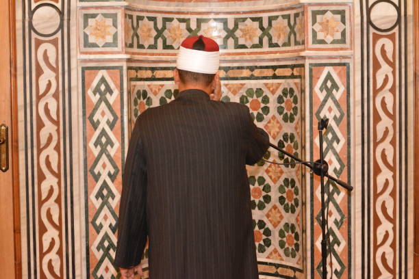 a mosque imam preacher muezzin in front of the microphone reciting adhan azan or calling loudly for the prayer or salah summoning muslims to enter the mosque - adhan imagens e fotografias de stock