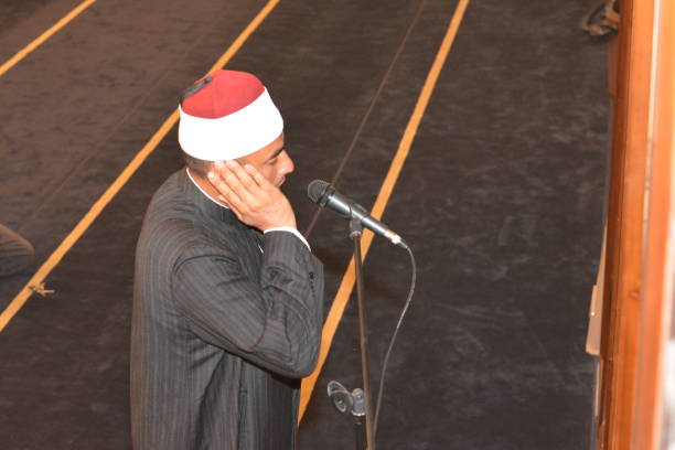 a mosque imam preacher muezzin in front of the microphone reciting adhan azan or calling loudly for the prayer or salah summoning muslims to enter the mosque - adhan imagens e fotografias de stock