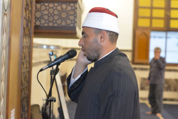 a mosque imam preacher muezzin in front of the microphone reciting adhan azan or calling loudly for the prayer or salah summoning muslims to enter the mosque - adhan imagens e fotografias de stock