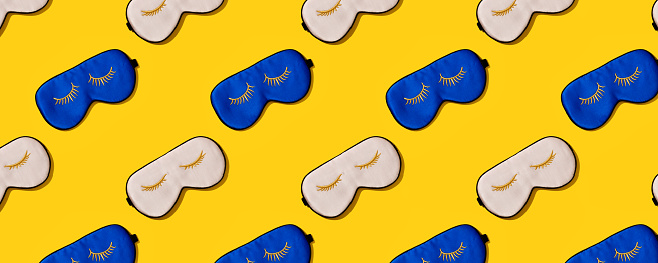 Sleeping mask pattern. Pink and blue silk sleeping masks for eyes on yellow background. Creative Top view Flat lay. Concept eye protection from light for good sleep and melatonin production.