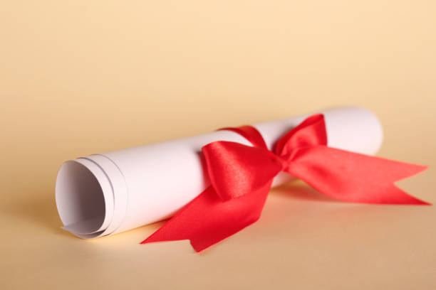 istock Rolled student's diploma with red ribbon on beige background 1411384930