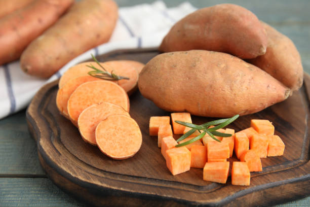 wooden board with cut and whole sweet potatoes on table, closeup - zoete aardappel fotos stockfoto's en -beelden