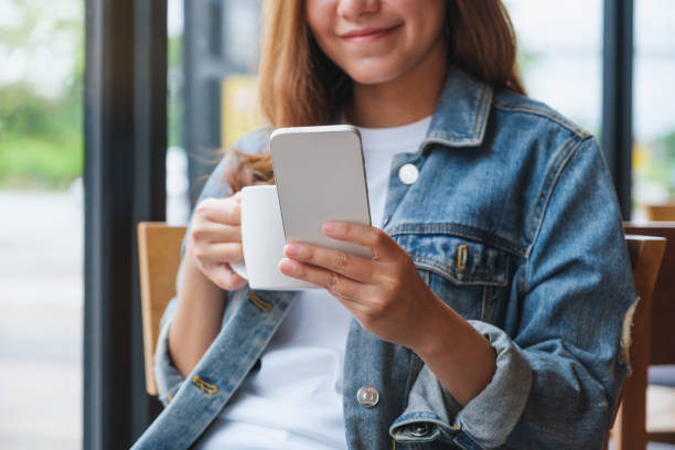istock Closeup image of a young woman holding and using mobile phone while drinking coffee in cafe 1411385143