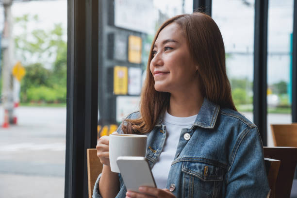 istock Portrait image of a young woman holding and using mobile phone while drinking coffee in cafe 1411385145
