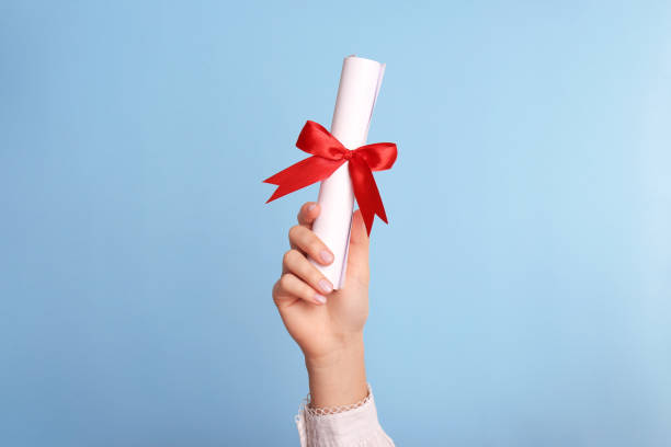 istock Student holding rolled diploma with red ribbon on light blue background, closeup 1411385191