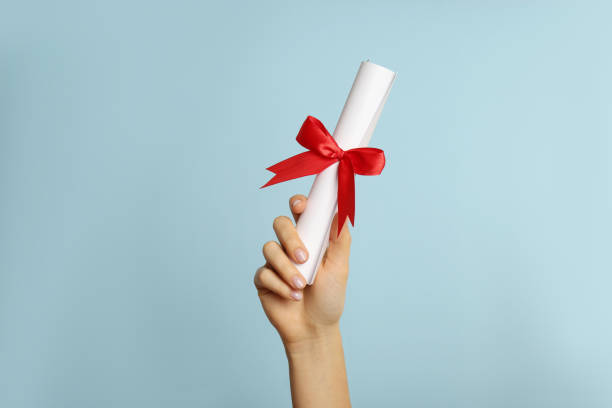 istock Student holding rolled diploma with red ribbon on light blue background, closeup 1411385192