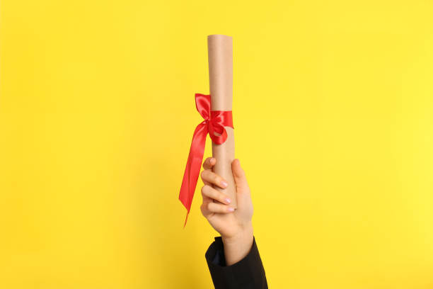istock Student holding rolled diploma with red ribbon on yellow background, closeup 1411385198