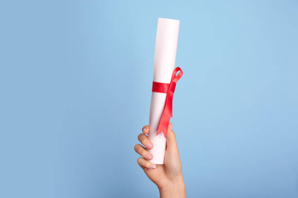 istock Student holding rolled diploma with red ribbon on light blue background, closeup 1411385540