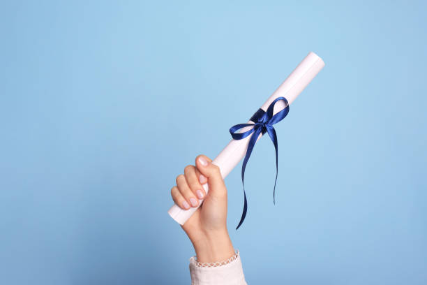 istock Student holding rolled diploma with ribbon on light blue background, closeup 1411385610