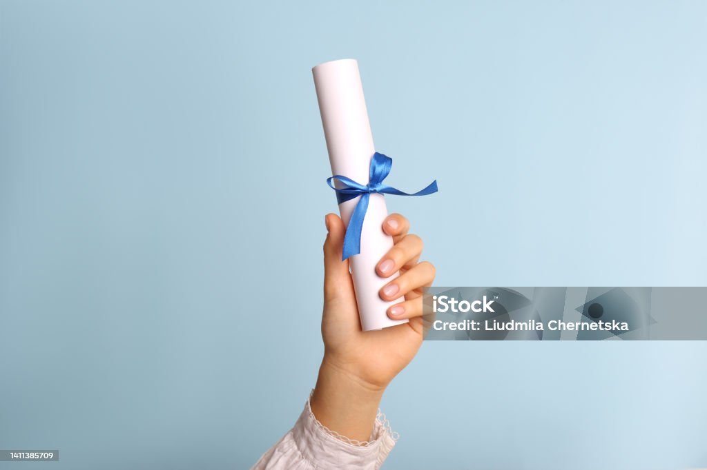Student holding rolled diploma with ribbon on light blue background, closeup Certificate Stock Photo