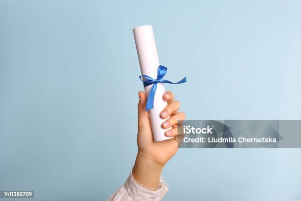 Student Holding Rolled Diploma With Ribbon On Light Blue Background Closeup Stock Photo - Download Image Now