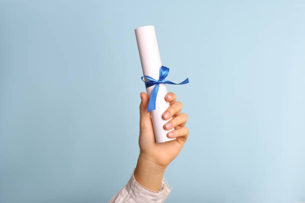 student holding rolled diploma with ribbon on light blue background, closeup - degree imagens e fotografias de stock