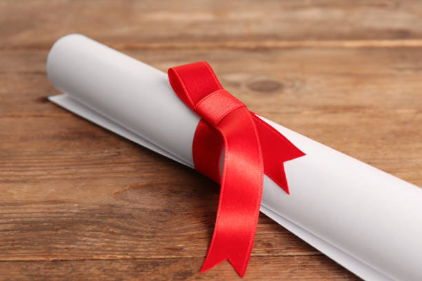 istock Rolled student's diploma with red ribbon on wooden table, closeup 1411385782