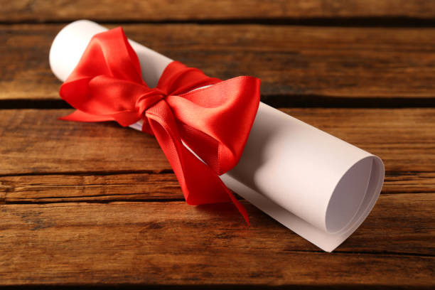 istock Rolled student's diploma with red ribbon on wooden table 1411385883