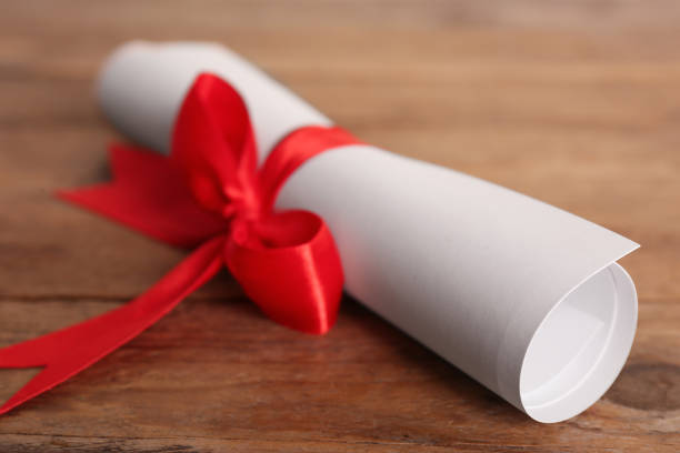 istock Rolled student's diploma with red ribbon on wooden table, closeup 1411385902
